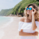 Haarpflege nach dem Strandurlaub - junge Frau mit Sonnenbrille am Strand.