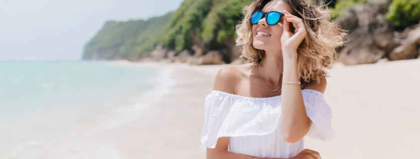 Haarpflege nach dem Strandurlaub - junge Frau mit Sonnenbrille am Strand.